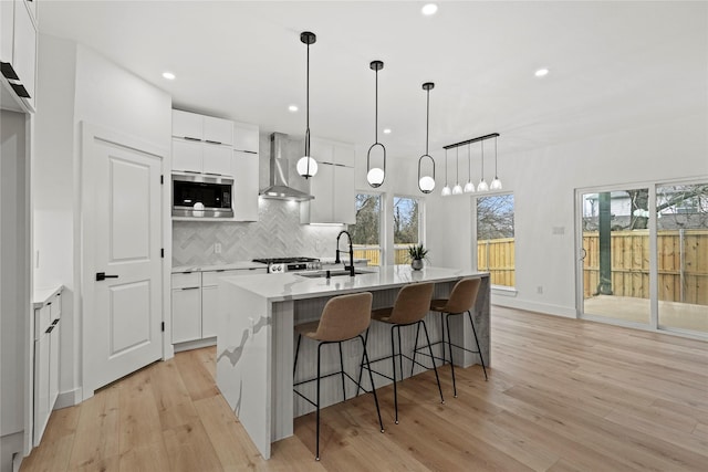 kitchen featuring stainless steel microwave, wall chimney range hood, and white cabinets