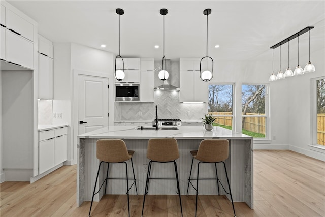 kitchen with white cabinetry, sink, stainless steel microwave, and an island with sink