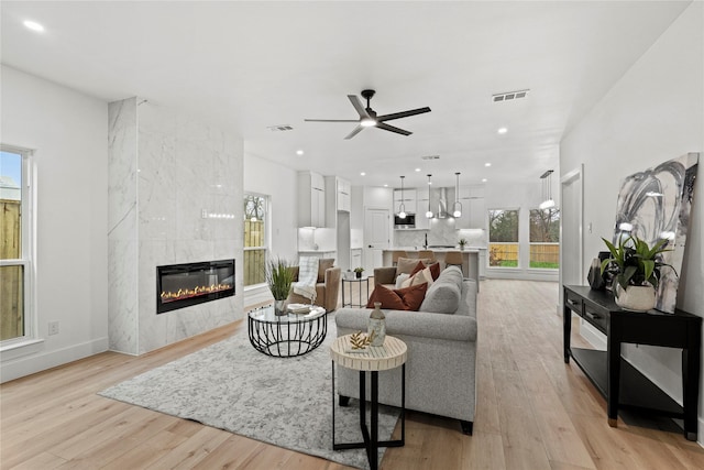 living room featuring ceiling fan, a high end fireplace, and light hardwood / wood-style floors