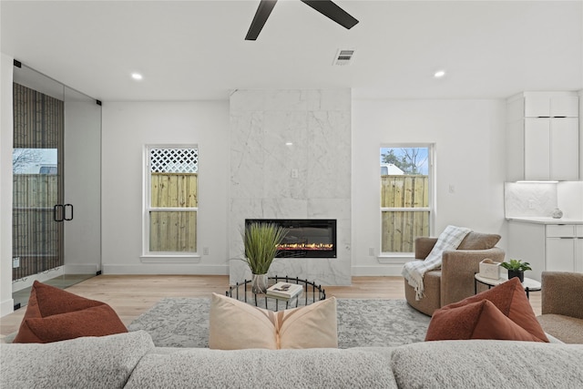 living room featuring a tiled fireplace, ceiling fan, and light wood-type flooring