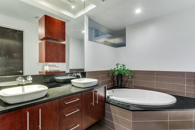 bathroom featuring a relaxing tiled tub and vanity