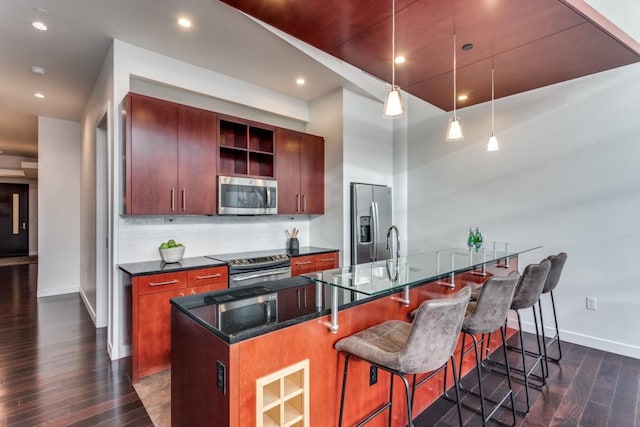 kitchen with hanging light fixtures, backsplash, stainless steel appliances, a center island with sink, and dark hardwood / wood-style flooring