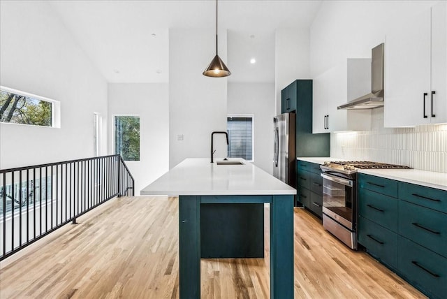 kitchen with pendant lighting, wall chimney range hood, sink, white cabinetry, and stainless steel appliances