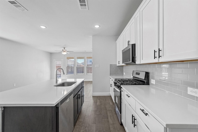 kitchen with sink, white cabinets, decorative backsplash, stainless steel appliances, and a center island with sink