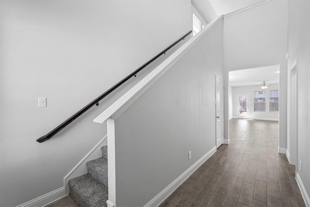 stairway with ceiling fan, wood-type flooring, and a high ceiling