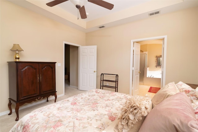 bedroom with connected bathroom, light colored carpet, ceiling fan, and a tray ceiling