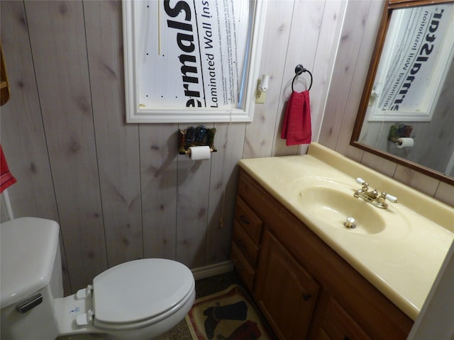 half bath featuring toilet, wood walls, and vanity