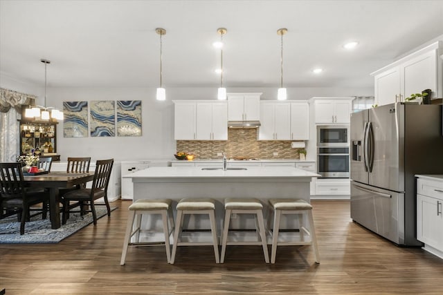 kitchen with pendant lighting, stainless steel appliances, and a center island with sink