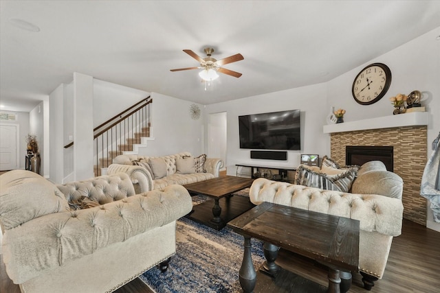 living room featuring ceiling fan, dark hardwood / wood-style floors, and a stone fireplace