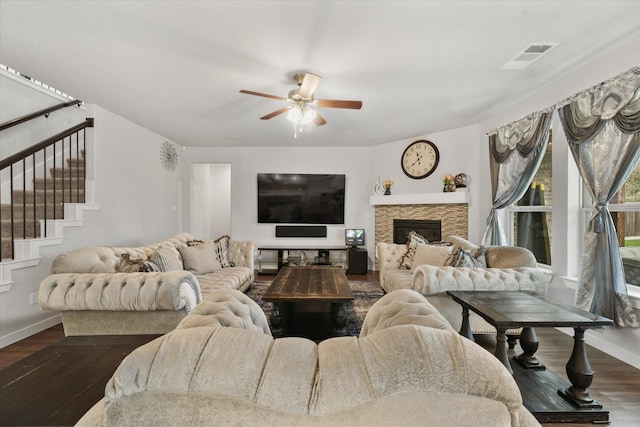 living room featuring ceiling fan, dark hardwood / wood-style floors, and a stone fireplace