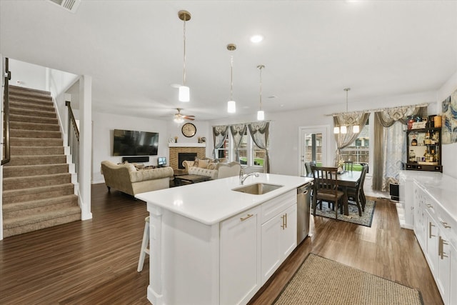 kitchen with pendant lighting, sink, dishwasher, white cabinetry, and an island with sink