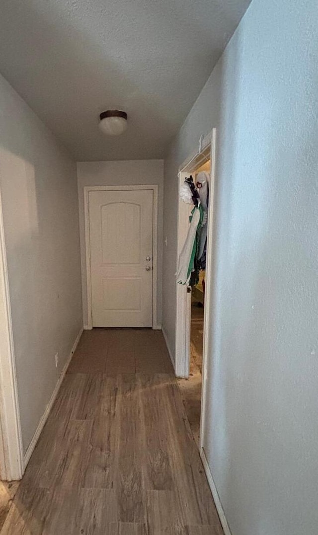 hallway with a textured ceiling, wood finished floors, and baseboards