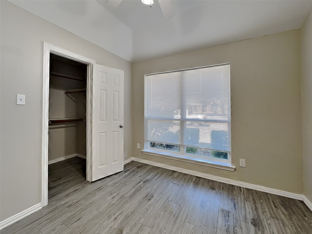 unfurnished bedroom featuring vaulted ceiling, a spacious closet, ceiling fan, light wood-type flooring, and a closet