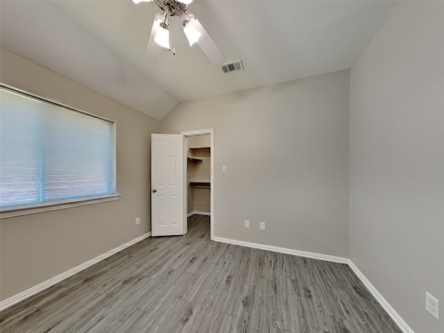 unfurnished bedroom featuring lofted ceiling, a walk in closet, ceiling fan, light wood-type flooring, and a closet