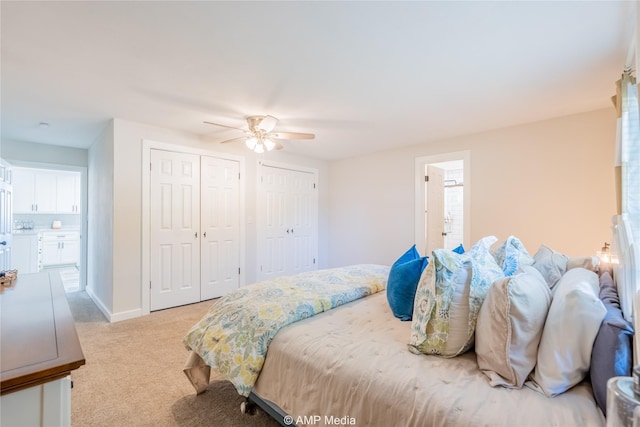 bedroom featuring multiple closets, ceiling fan, ensuite bathroom, and light carpet