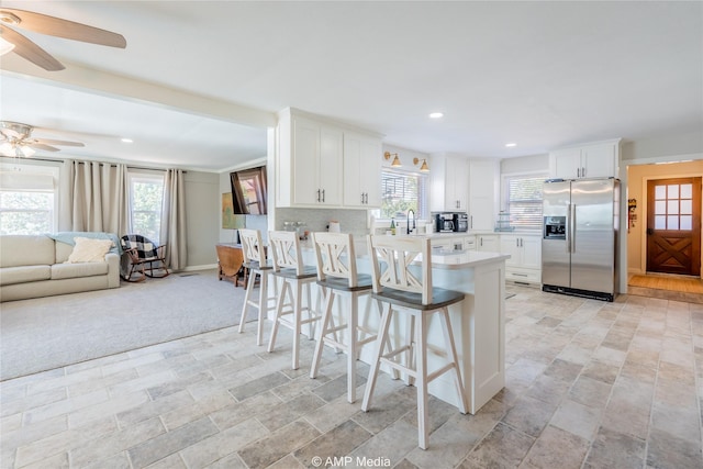 kitchen with a breakfast bar area, white cabinetry, stainless steel fridge with ice dispenser, ceiling fan, and decorative backsplash