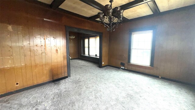 spare room with beamed ceiling, plenty of natural light, wooden walls, and carpet floors