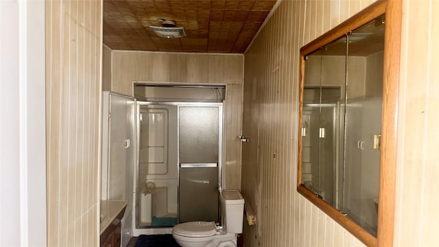 bathroom with a shower with shower door, wood walls, and toilet