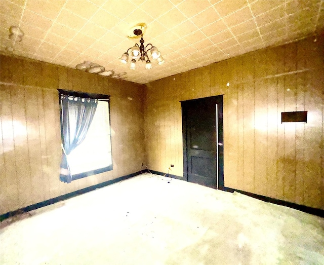 empty room featuring a notable chandelier and wooden walls