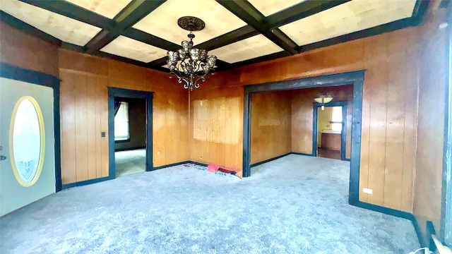 empty room featuring coffered ceiling, beam ceiling, light colored carpet, and wood walls