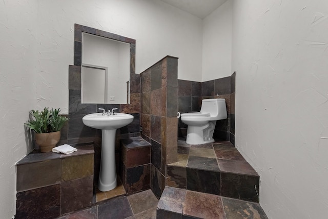 bathroom with toilet, sink, and tile walls