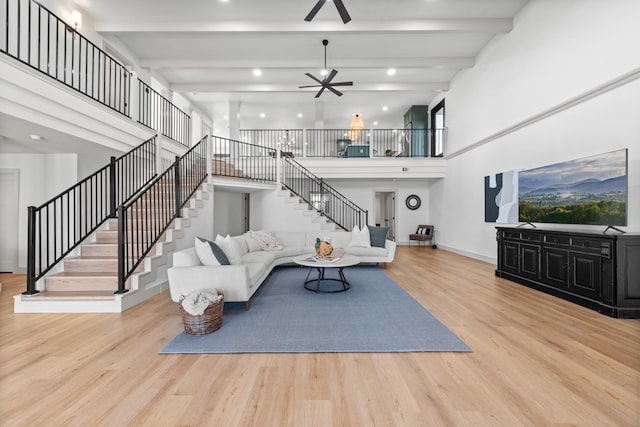 living room with ceiling fan, beam ceiling, a high ceiling, and light wood-type flooring