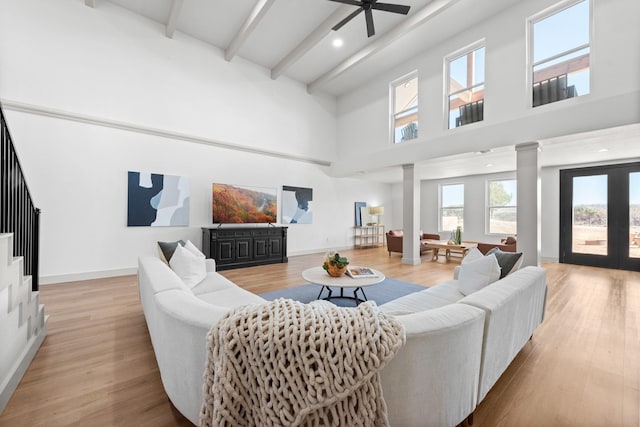 living room featuring a towering ceiling, light hardwood / wood-style flooring, beamed ceiling, and ornate columns