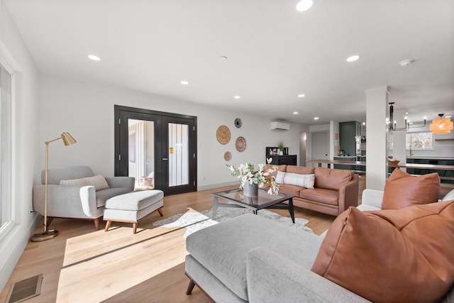 living room featuring french doors, an inviting chandelier, light hardwood / wood-style flooring, and an AC wall unit