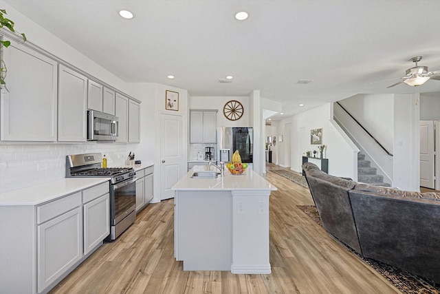 kitchen featuring stainless steel appliances, a kitchen island with sink, sink, and light hardwood / wood-style flooring