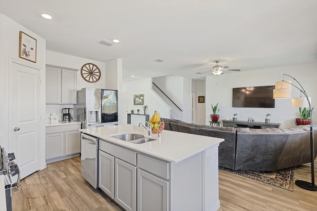 kitchen featuring sink, gray cabinetry, light wood-type flooring, appliances with stainless steel finishes, and a kitchen island with sink