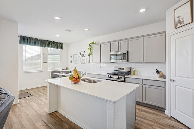 kitchen featuring sink, gray cabinets, stainless steel appliances, and a center island with sink