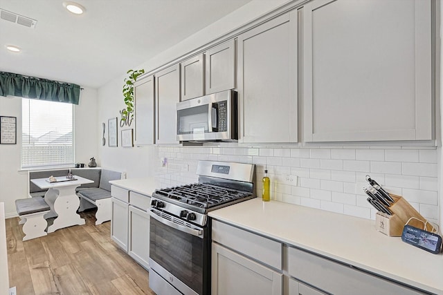 kitchen featuring stainless steel appliances, light hardwood / wood-style floors, decorative backsplash, and gray cabinetry