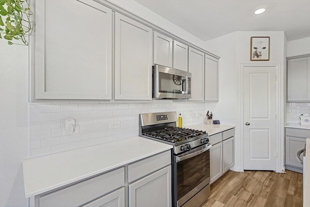 kitchen with appliances with stainless steel finishes, gray cabinets, decorative backsplash, and light wood-type flooring