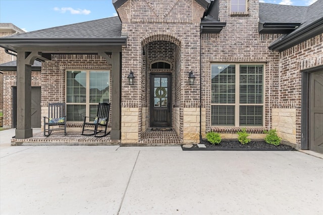 entrance to property featuring a shingled roof, brick siding, and a porch