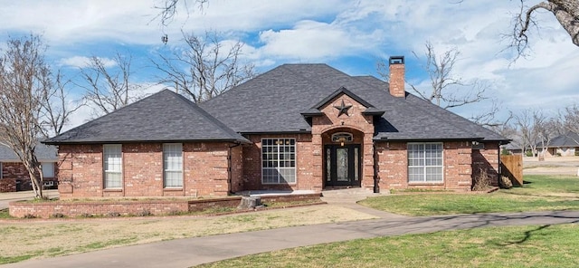 view of front facade featuring brick siding, a chimney, and a shingled roof