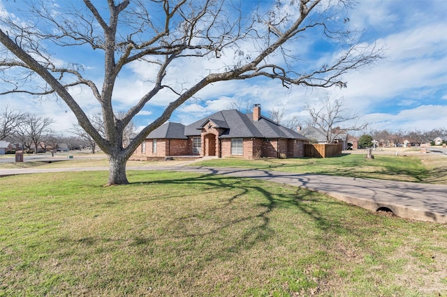 view of front of house with brick siding, concrete driveway, a chimney, and a front yard