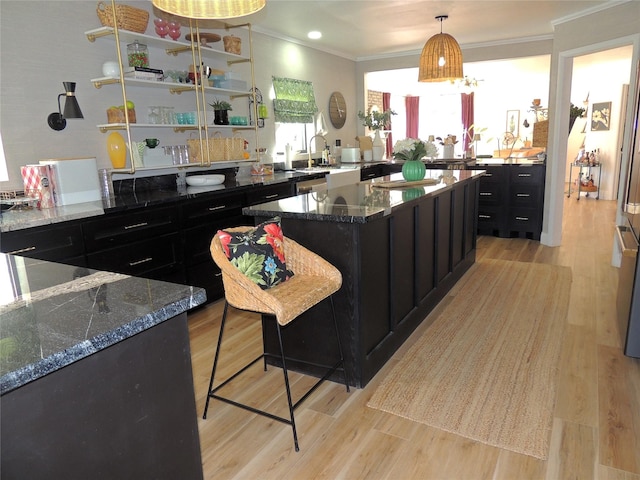 kitchen featuring crown molding, a kitchen breakfast bar, a kitchen island, dark stone counters, and light wood-type flooring