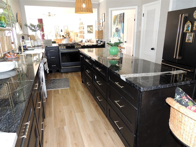 kitchen with dark stone counters, stainless steel range with gas stovetop, a center island, and light hardwood / wood-style floors