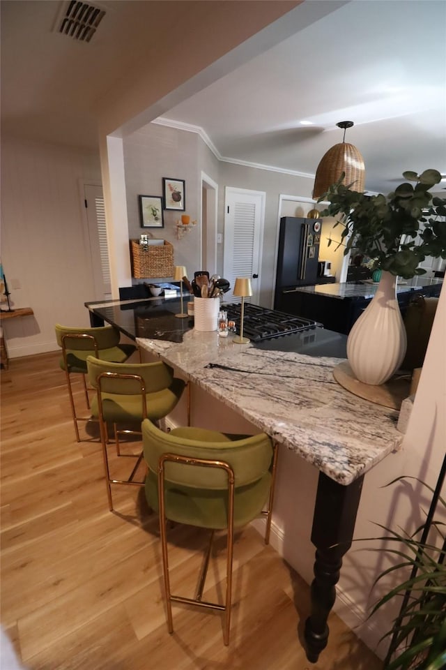 bar with light stone counters, high end black fridge, crown molding, and light hardwood / wood-style floors