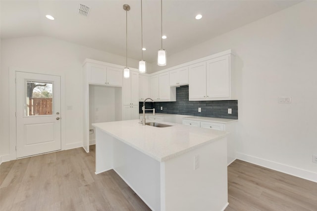 kitchen featuring sink, a center island with sink, pendant lighting, decorative backsplash, and white cabinets