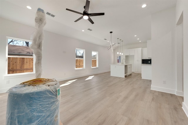 unfurnished living room with plenty of natural light, sink, ceiling fan with notable chandelier, and light hardwood / wood-style flooring