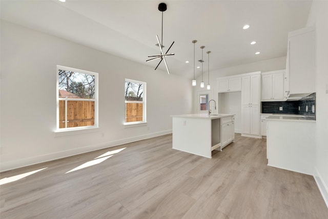 kitchen featuring decorative light fixtures, white cabinetry, an island with sink, decorative backsplash, and light hardwood / wood-style flooring