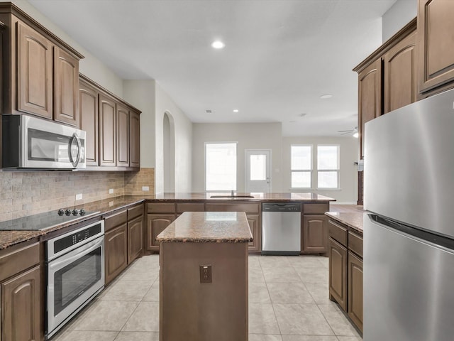 kitchen with light tile patterned floors, a peninsula, a sink, stainless steel appliances, and backsplash