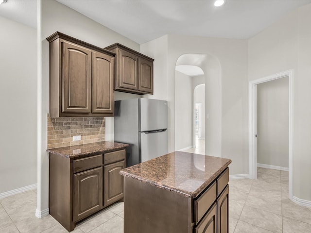 14824 Angel Trace Dr, Aledo, TX 76008 - kitchen featuring baseboards, dark stone counters, arched walkways, freestanding refrigerator, and backsplash