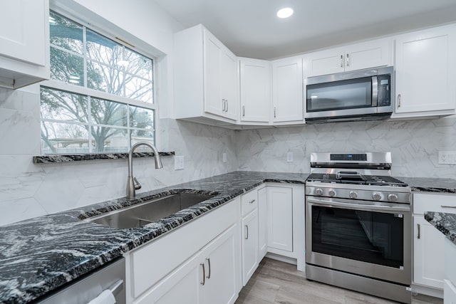 kitchen featuring sink, stainless steel appliances, dark stone counters, and white cabinets