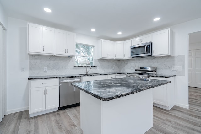 kitchen with appliances with stainless steel finishes, sink, white cabinets, dark stone counters, and a center island