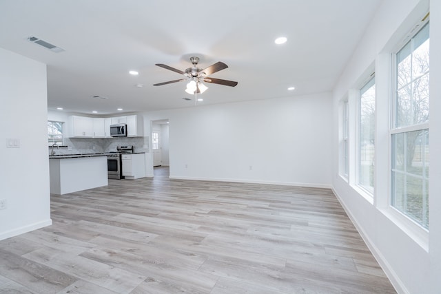 unfurnished living room with ceiling fan, plenty of natural light, sink, and light hardwood / wood-style floors