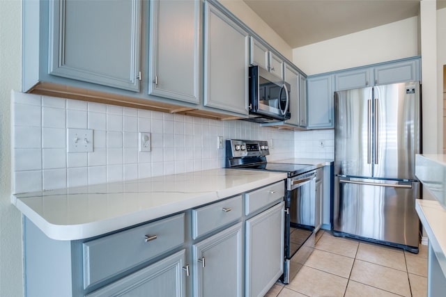 kitchen with tasteful backsplash, gray cabinetry, stainless steel appliances, and light tile patterned floors