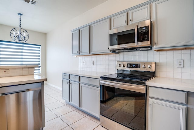 kitchen with tasteful backsplash, stainless steel appliances, hanging light fixtures, and gray cabinetry