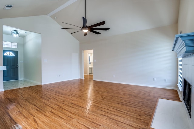 unfurnished living room with ceiling fan, a tiled fireplace, high vaulted ceiling, and light hardwood / wood-style flooring